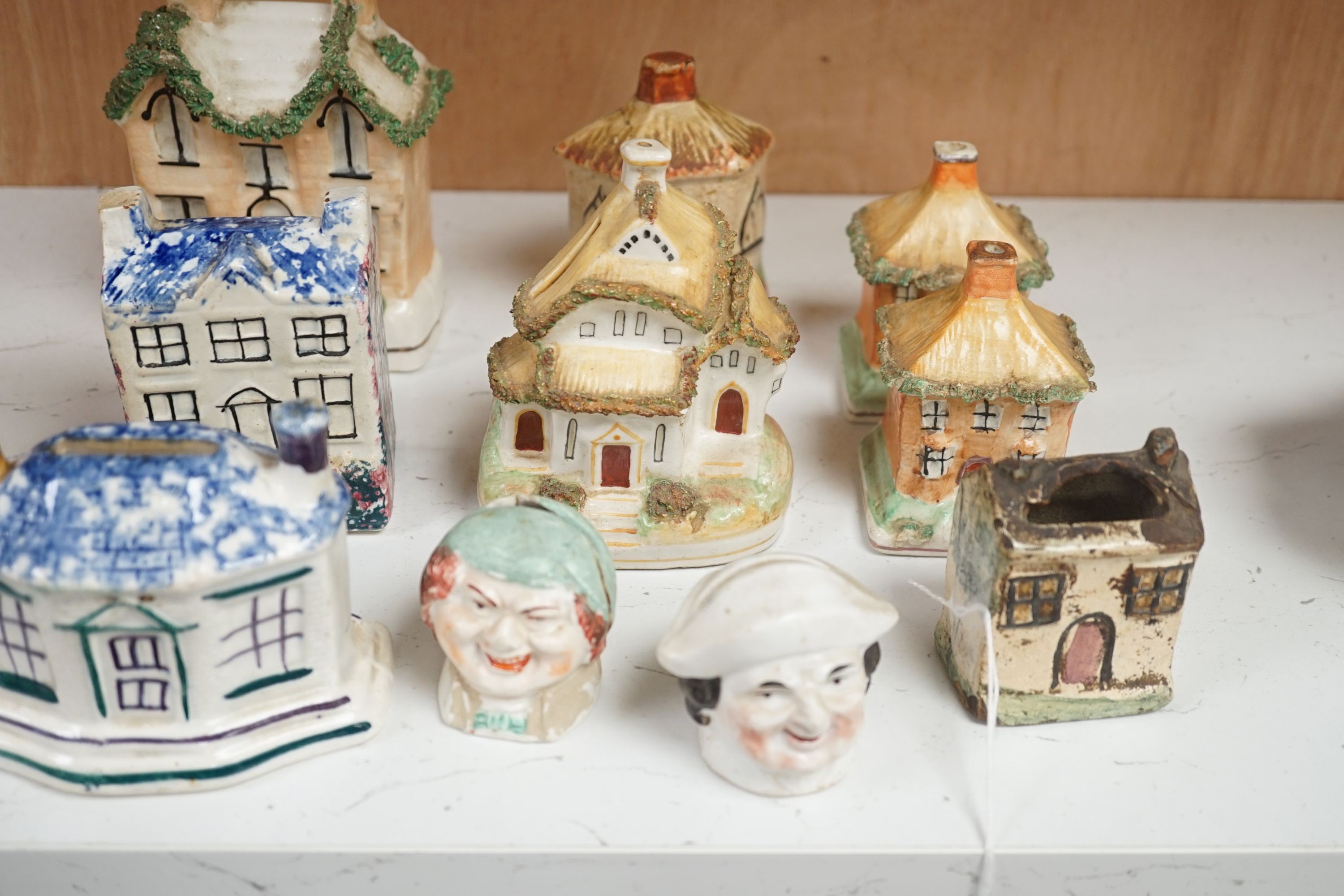 Twelve Staffordshire pottery money boxes, three with sponged decoration, modelled as cottages or heads, tallest 13.5 cms high.